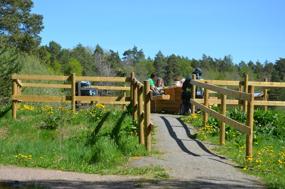 En liten grusväg med staket på sidorna leder upp till rastbord där en grupp fikar.