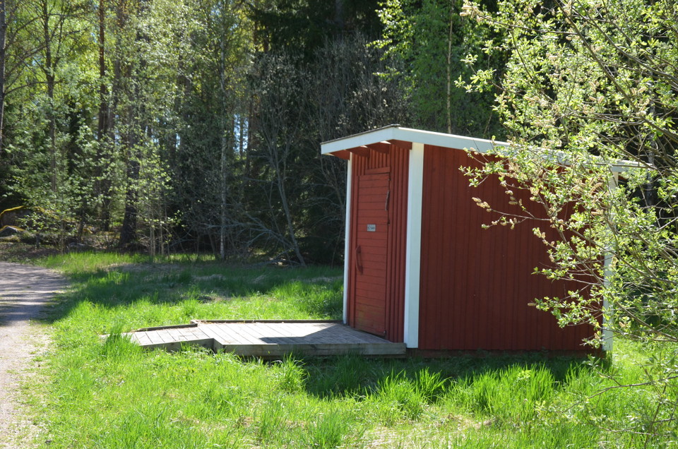 Bild på utedass vid en smal grusväg.
