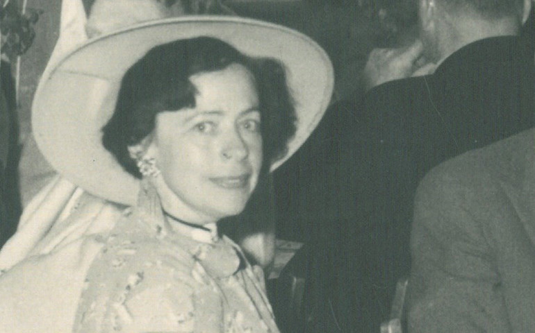 Elfriede Meyer-Rosskam tittar in i kameran och ler svagt. Hon har en stor hatt på huvudet och klänning.