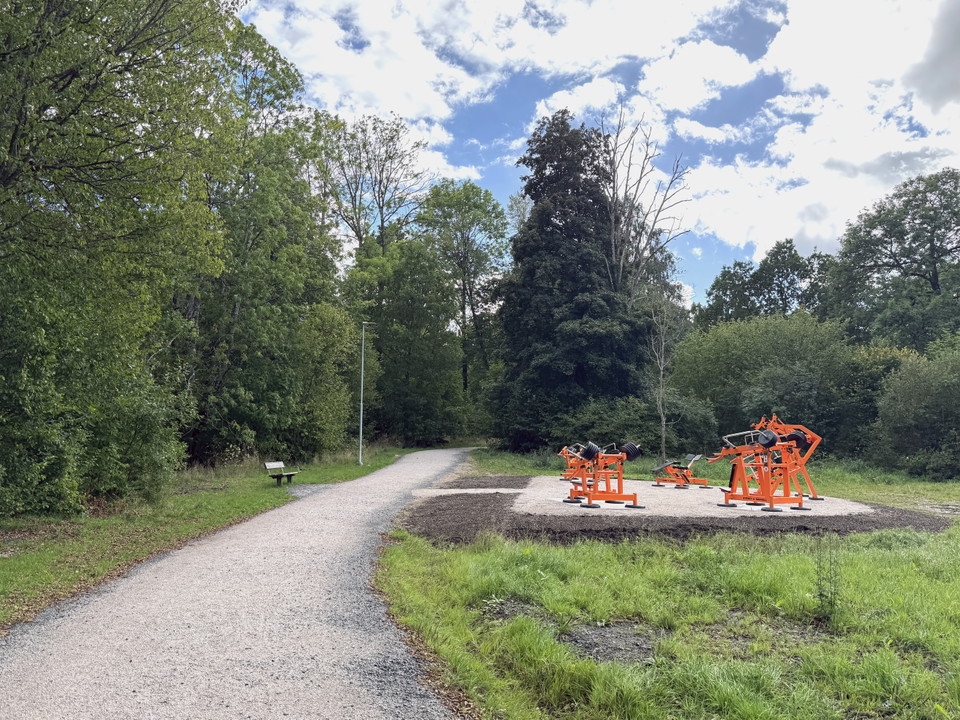 Fem träningsmaskiner står i grupp intill ett motionsspår. Runt omkring syns skog.