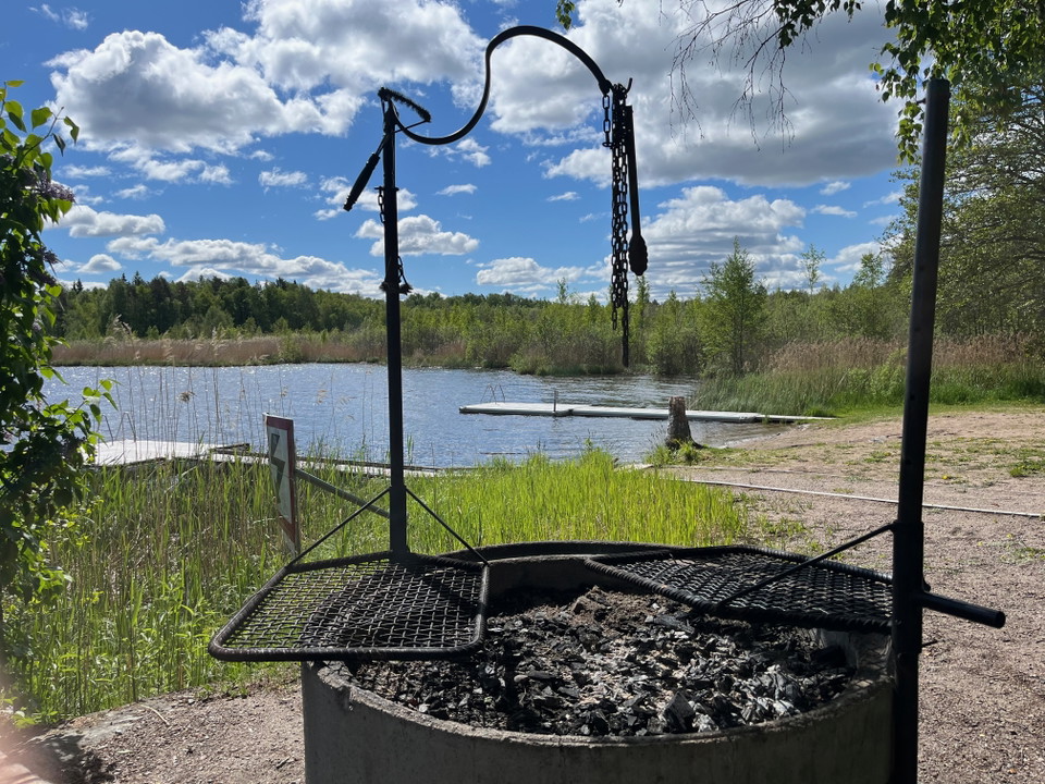 Närbild på en grill med två grillgaller, i bakgrunden syns en strand och vatten.