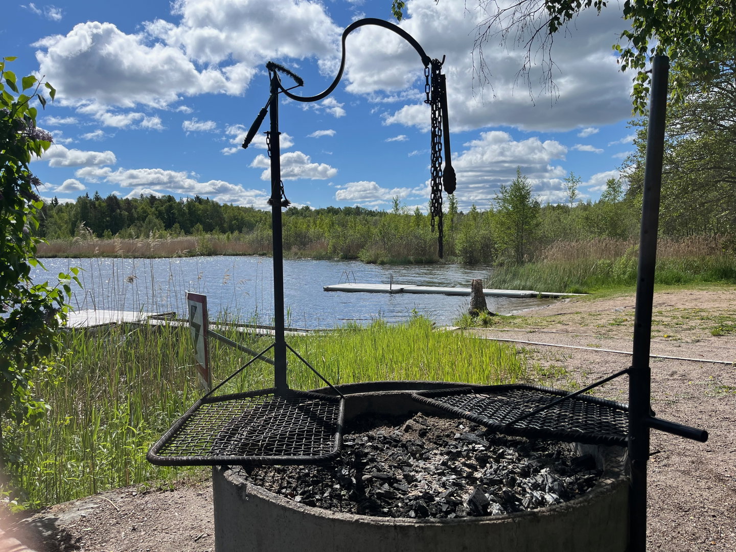Närbild på en grill med två grillgaller, i bakgrunden syns en strand och vatten.