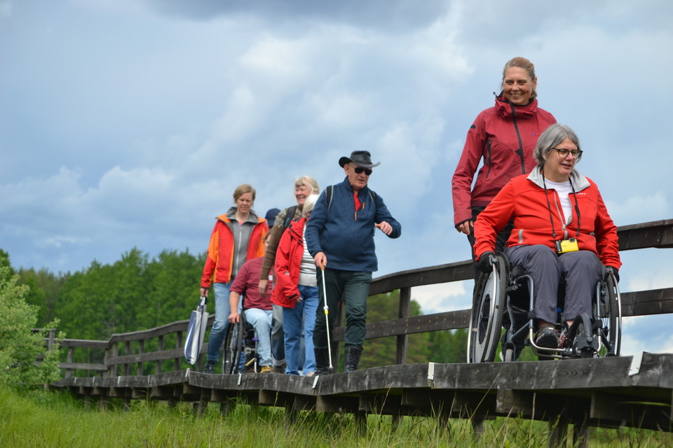 Flera människor på en spång, några med rullstol, en man har vit käpp.