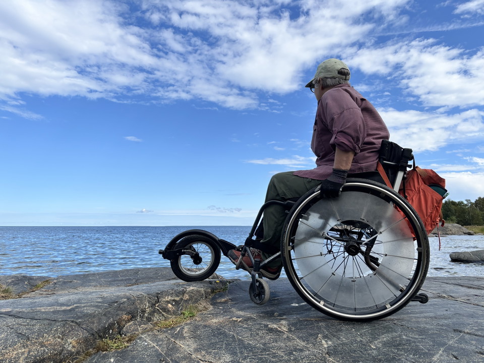 Kvinna i rullstol på klippa vid vatten.