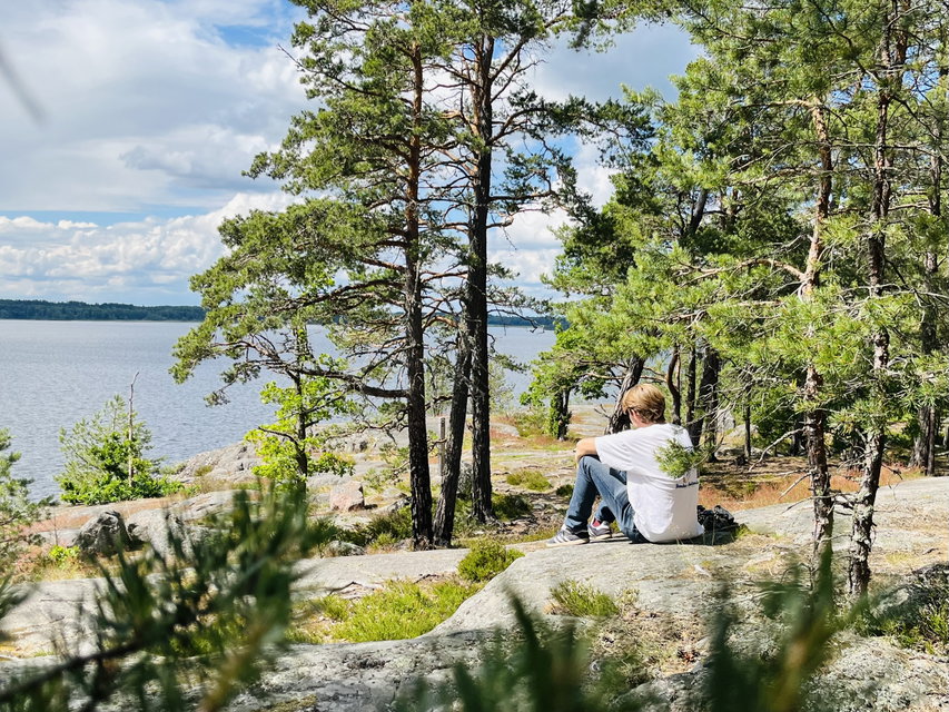 En person sitter på en klippa och tittar ut över vattnet. 