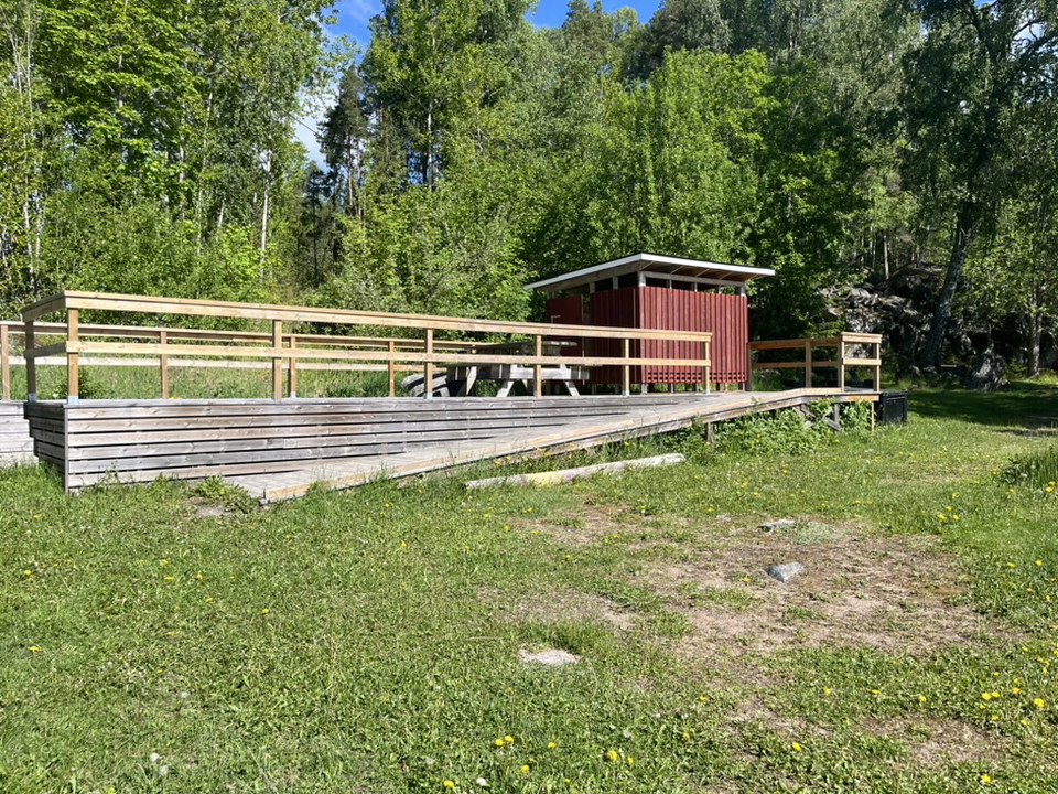 En ramp leder upp till ett trädäck där det står en liten röd byggnad.