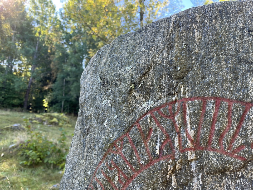 Närbild på en runsten, en grå sten med rödmålade runor.