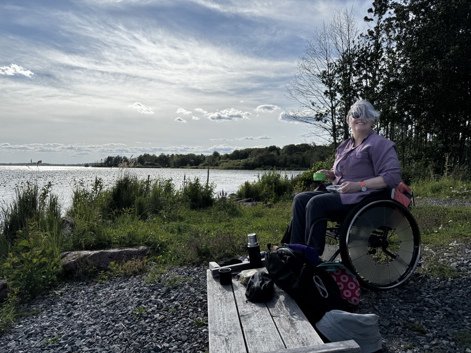 En kvinna i rullstol har picknick vid vatten.