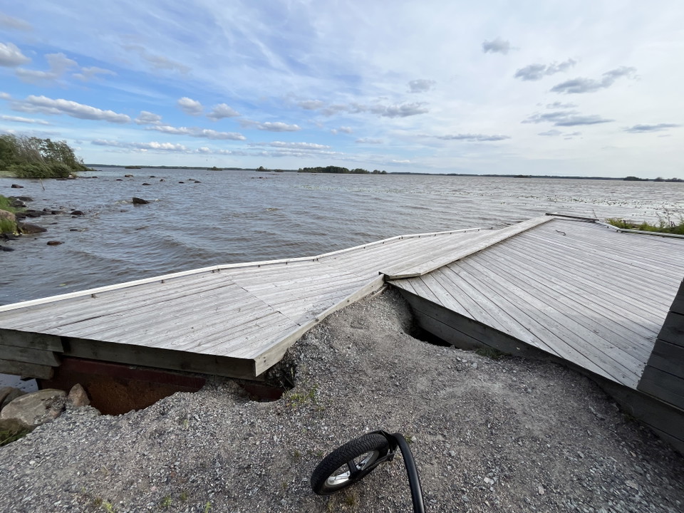 Bild visar brygga vid vatten med grus och djupa hål.