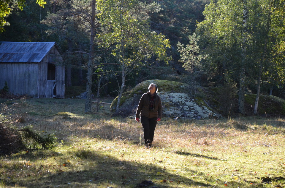 En kvinna går på en äng med en lada i bakgrunden.