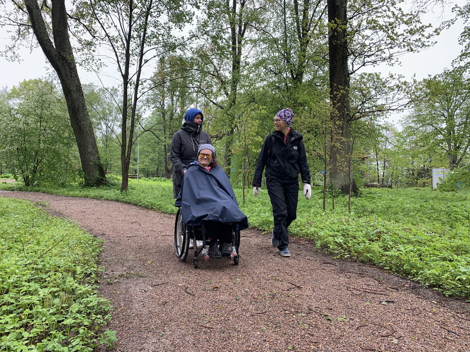 Hårdgjord stig i parkmiljö. Två personer går och en åker rullstol.