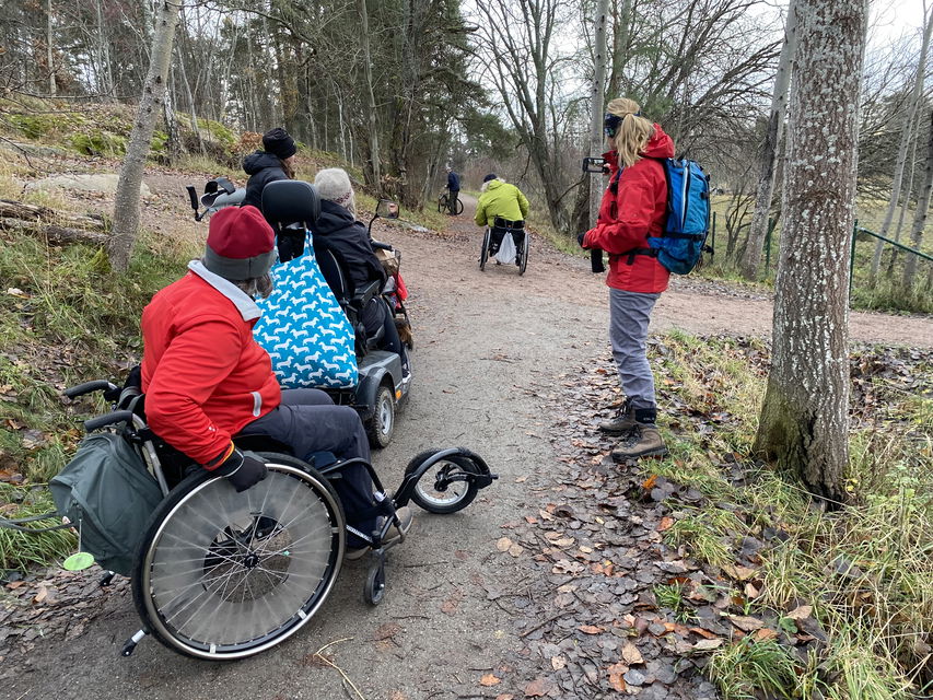 Flera personer i rullstol. En som kör  på stig med lutning. Höstbild.