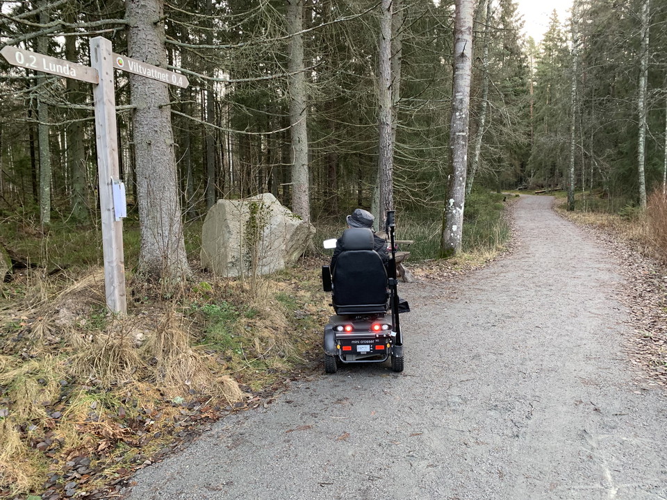 En person i elrullstol tittar på vägvisare vid stigen