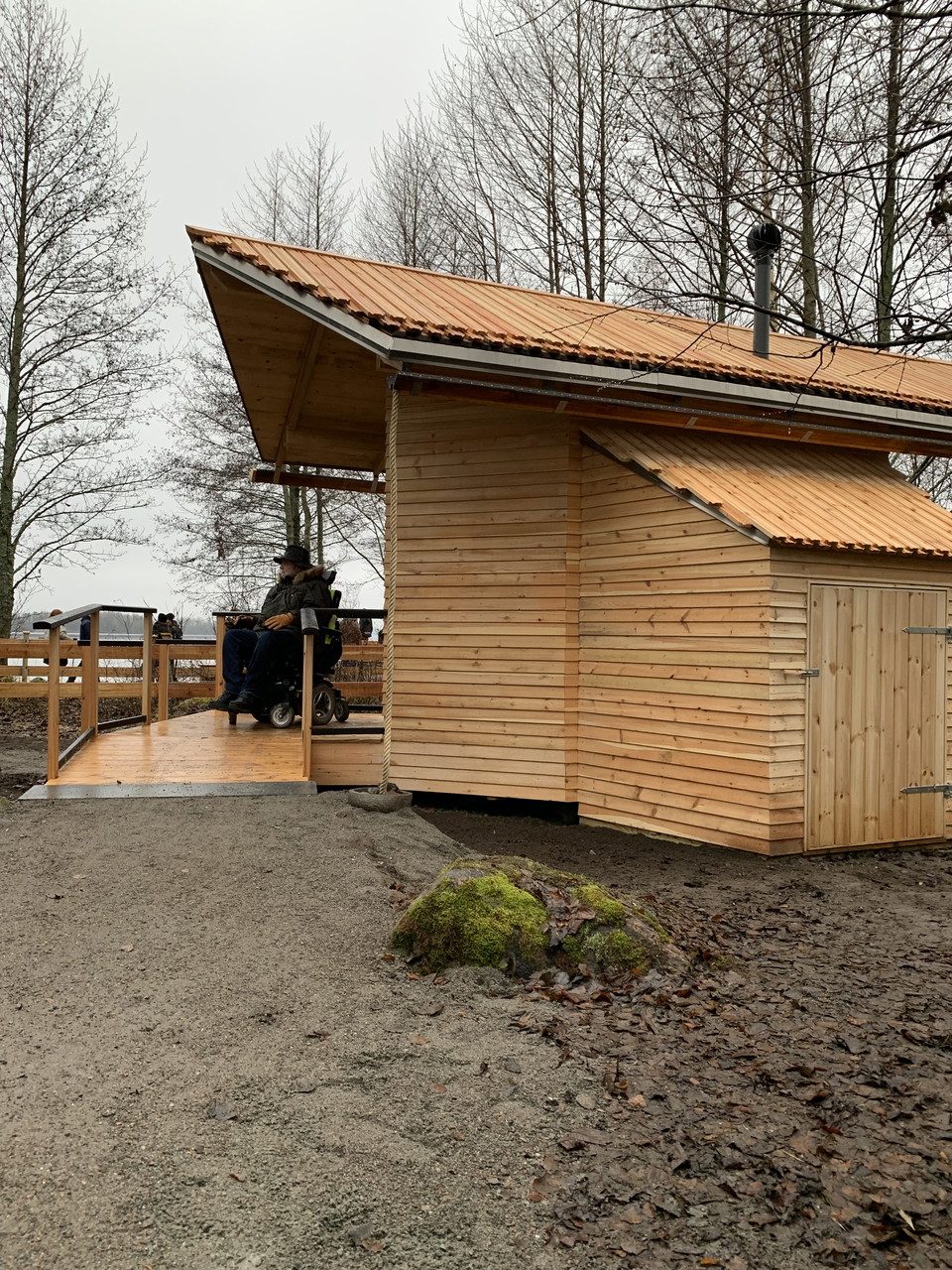 En man i rullstol bredvid en träbyggnad.